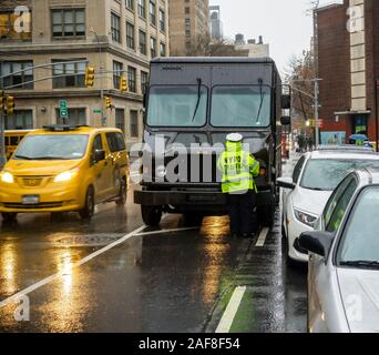 A UPS truck double-parked in Chelsea in New York receives a ticket from an NYPD traffic agent on Monday, December 9, 2019. The New York City Council is considering a bill that would end the Stipulated Fine Program which enables a negotiated settlement with New York’s 10 largest shippings that reduce their  fines. (© Richard B. Levine) Stock Photo