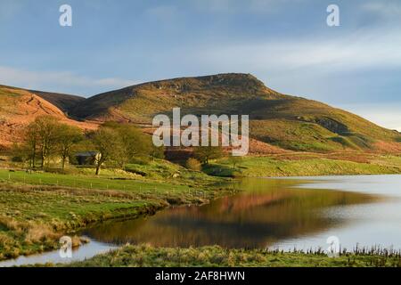 Scenic morning rural view (Embsay Reservoir, steep sunlit fells or moors, summit of high upland hill & crag, blue sky) - North Yorkshire, England, UK.