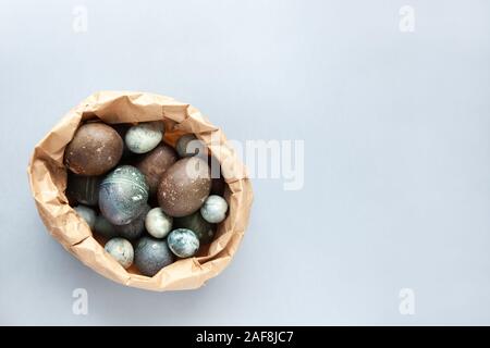 Creatively painted chicken and quail Easter eggs with natural hibiscus dye, look like sea stones in craft bag on a gray background. Happy Easter DIY c Stock Photo
