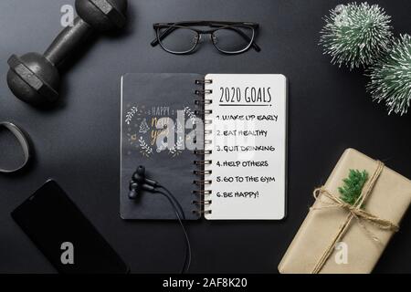 New Year Healthy Goals and Resolutions concept. 2020 New Year's Goals written on  Notebook Paper, and dumbbells on black Background, Fitness, Sport an Stock Photo