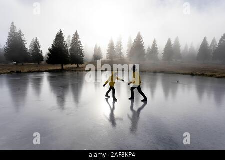Mother and son playing, walking on ice on frozen mountain lake at autumn meadow, Velika planina, Slovenia Stock Photo