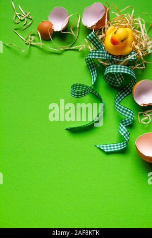 Yellow rubber duck in a straw nest, broken eggshell and green checkered ribbon, minimalistic easter background or concept Stock Photo