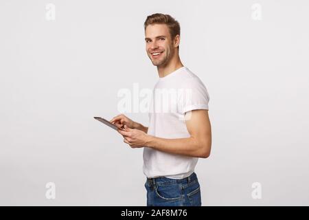 Attractive blond male office assistant, manager, using digital tablet to input or record information, using corporate application, standing profile Stock Photo