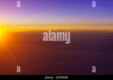 The rising sun illuminates the clouds above the earth. Dawn above the clouds. The view from the window of the plane. Stock Photo