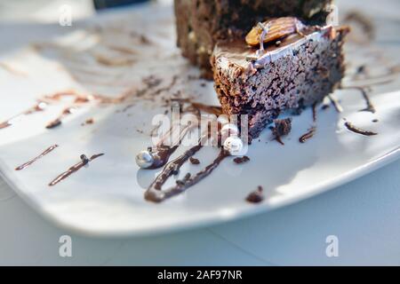 Detail of a chocolate cake with chocolate sauce, on a white plate, which is decorated with small silver balls. Close up with very soft background in b Stock Photo