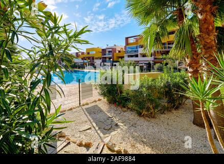 Luxury dwelling residential houses multicoloured homes through lush tropical plants leaves, public swimming pool view at sunny day. Torrevieja, Spain Stock Photo