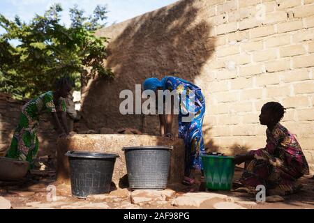 Black African Women Pouring Water into Bucket Stock Photo