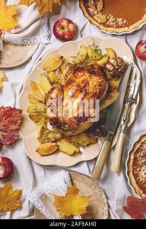 Thanksgiving or Halloween dinner with baked chicken with potatoes and lemons on big ceramic dish, pumpkin pies, plates, yellow autumn leaves, pumpkins Stock Photo