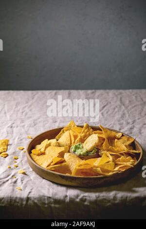 Tortilla nachos corn chips with avocado guacamole sauce served in wood plate on linen table cloth. Mexican snack Stock Photo