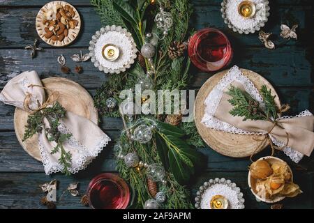 Christmas or New year table setting with empty ceramic plates, wine glasses, napkins, Christmas thuja wreath, luminous garland and burning candles on Stock Photo