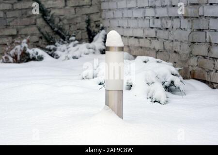 Lantern to illuminate the track at the cottage in winter. Cylindrical garden lamp on a white snow background. Solar powered LED garden park lamp. Stock Photo