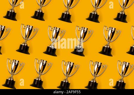 Champion cups on yellow background as pattern. Flat lay style. Open composition. Stock Photo