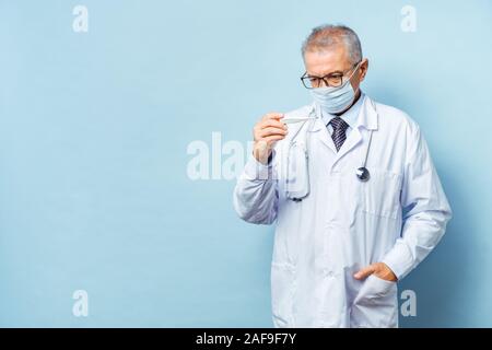 Portrait of a handsome senior doctor holding a thermometer in his hands, on a thermometer, the normal temperature of a healthy person is 36.6 degrees Stock Photo