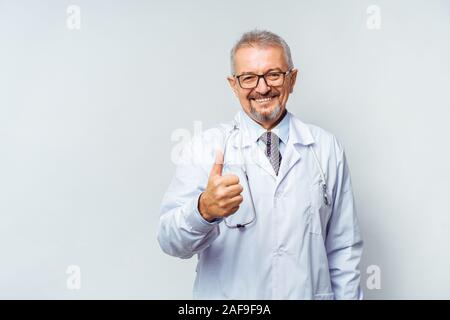 Smiling medical senior doctor with a stethoscope. On a blue background. Medic shows thumb raised up. The concept of humanity's victory over disease Stock Photo