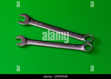A pair of stainless steel wrenches, combination spanners with both an open end and a box end, lie on a solid green background. their sizes are engrave Stock Photo