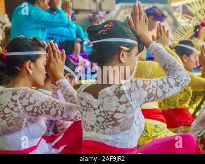 Ubud, Bali - Oct 12, 2012. A crowd of Hindu worshippers wearing traditional Balinese ceremonial clothing praying outdoors at a public temple. Stock Photo