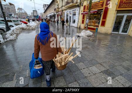 Bucharest, Romania - January 15, 2019: An elderly villager woman carries two baskets with traditional wooden tools for cooking. Stock Photo