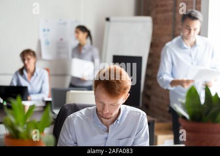 Employees working in shared office focus on busy redhead man Stock Photo