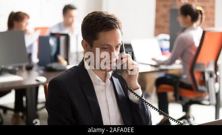 Company employee sitting in shared office talking on landline Stock Photo