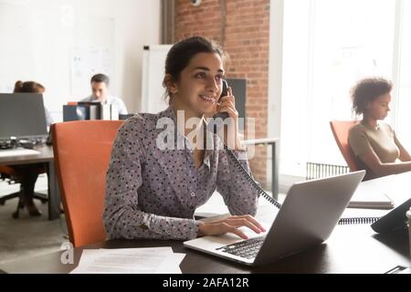 Indian woman sitting in coworking talking on phone with customer Stock Photo