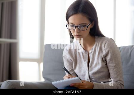Focused young woman in glasses make notes in notebook Stock Photo