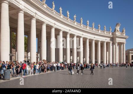 A line of visitors queue by Bernini's colonnade in St Peter's Square, waiting to get into St. Peter's Basilica, Rome Stock Photo