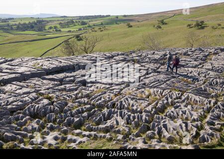 Two adults walk across the limsestone pavement at the top of Malham Cove in the Yorkshire Dales Stock Photo