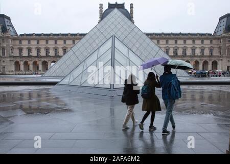 Visitors outside the glass pyramid entrance to the Louvre on a wet winter morning in Paris Stock Photo