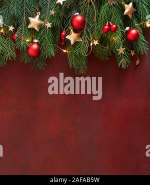 Christmas border with fir branches, red baubles and gold stars on the wooden board painted in dark-red with copy space for text. Flat lay. Christmas a Stock Photo