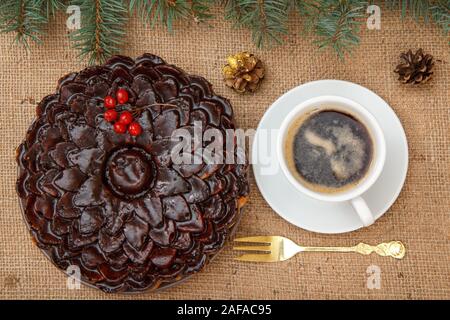Chocolate cake decorated with bunch of viburnum, cup of coffee with branch of spruce on table with branch of spruce, fork and sackcloth.