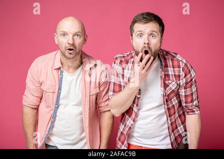 Portrait of two shocked young people who, from an unexpected surprise, opened their mouths and looked in surprise at the camera. Stock Photo