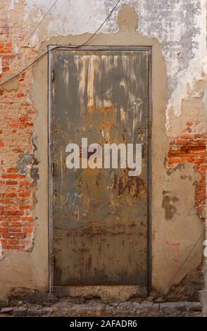 Closeup neglected vintage rusty steel door with wooden doorframe on brick wall with cement plaster Stock Photo