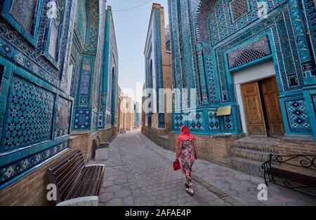 woman walks through narrow path through facades heavily decorated with blue tiles in necropolis Shah-i-Zinda, Samarqand, Uzbekistan, Central Asia