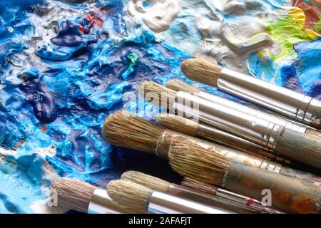 Old used paint brushes with wooden handles on palette with acryllic paint in different colours Stock Photo