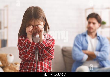 Little girl crying after quarrel wIth father, angry dad behind Stock Photo