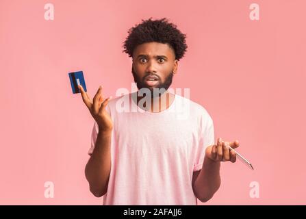 Confused black man holding credit card and cellphone Stock Photo