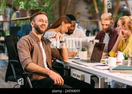 Love my job. Programmer smiling to camera, sitting in coworking office Stock Photo