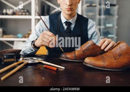 Bootmaker with brush tints shoes, footwear repair service. Craftsman ...