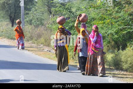 Rajasthani women in veil wear warm cloth and carry vessels on their head to collect drinking water from a village near Beawar. Photo/Sumit Saraswat Stock Photo