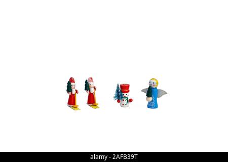 Small Christmas Figures isolated on white background. Two red Santa Clause toys wearing skis, a snowman and a blue angel all holding pine tree. Stock Photo