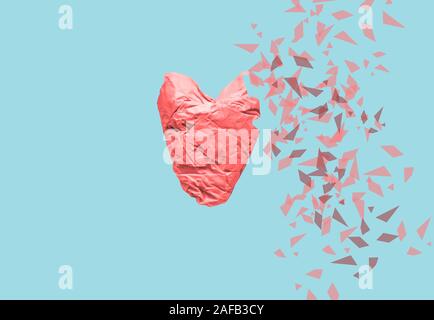 Delicate red heart made from crumpled paper partially torn to pieces on a gentle trendy blue background. The concept of fragility of the human heart Stock Photo