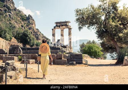 Young woman tourist at Sanctuary of Athena, Delphi Greece. Fashion white dress, large hat, yellow skirt Stock Photo