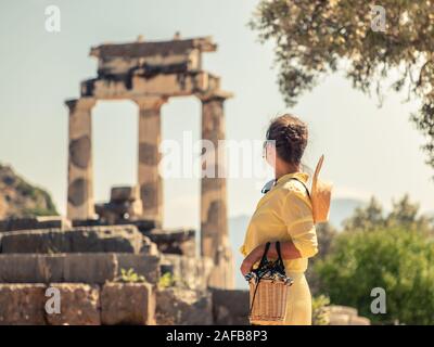 Young woman tourist at Sanctuary of Athena, Delphi Greece. Fashion white dress, large hat, yellow skirt Stock Photo