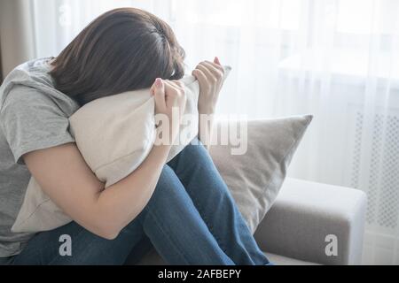 Sad depressed woman at home, she is sitting on the couch and hugging a pillow, loneliness and sadness concept Stock Photo