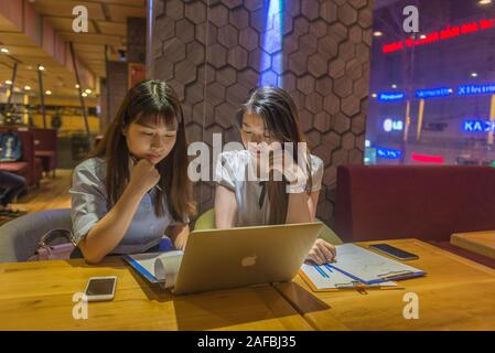 Two Asian businesswomen working on laptop and having discussion  Stock Photo