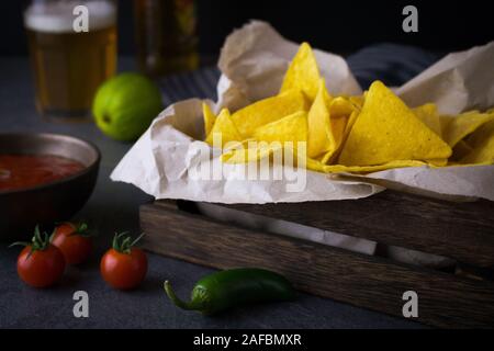 Food photography of a box with nachos or tortilla chips with salsa and guacamole dip and mexican beer or cerveza Stock Photo