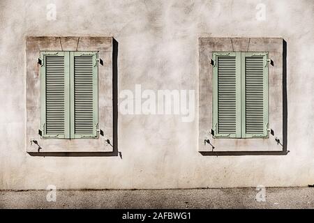 Two windows are closed with green wooden shutters in the town of Coustelet in Provence, France. Stock Photo