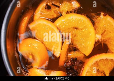 Making hot alcoholic mulled wine with oranges and spices. Christmas beverages boil in the metal pan. Glintwine from rose wine with citrus, cloves Stock Photo