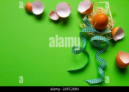 Brown chicken egg in a straw nest, broken eggshell and green checkered ribbon, minimalistic easter background or concept Stock Photo