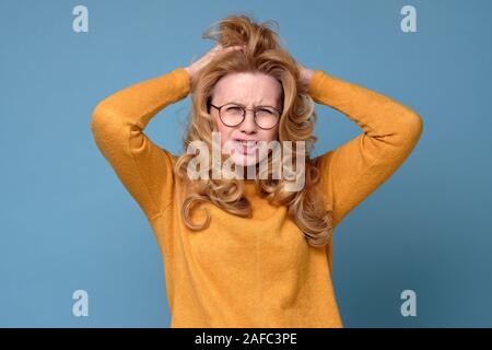 Mature caucasian woman in yellow sweater keeps hands on head, stares with terror Stock Photo